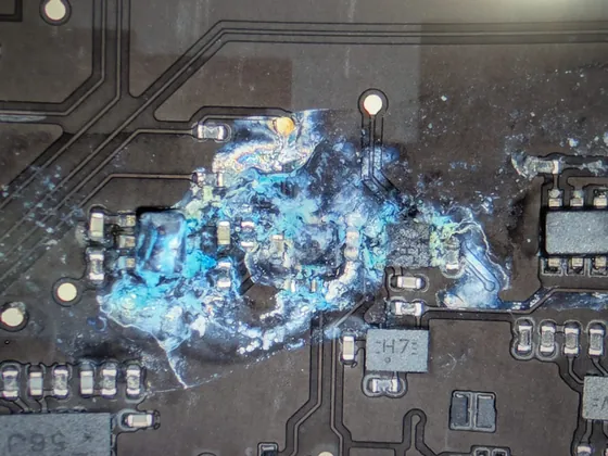 Coroziune masivă acoperind componentele și traseele de pe placa unui MacBook Pro M5, înainte de refacerea traseelor